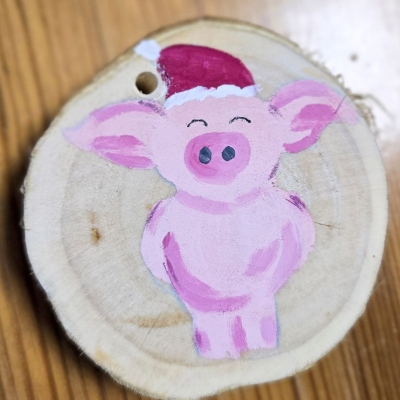Eine bemalte Deko-Holzscheibe mit einem Schwein mit Weihnachtsmütze