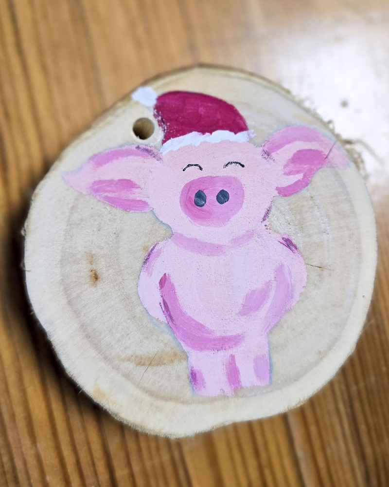 Eine bemalte Deko-Holzscheibe mit einem Schwein mit Weihnachtsmütze
