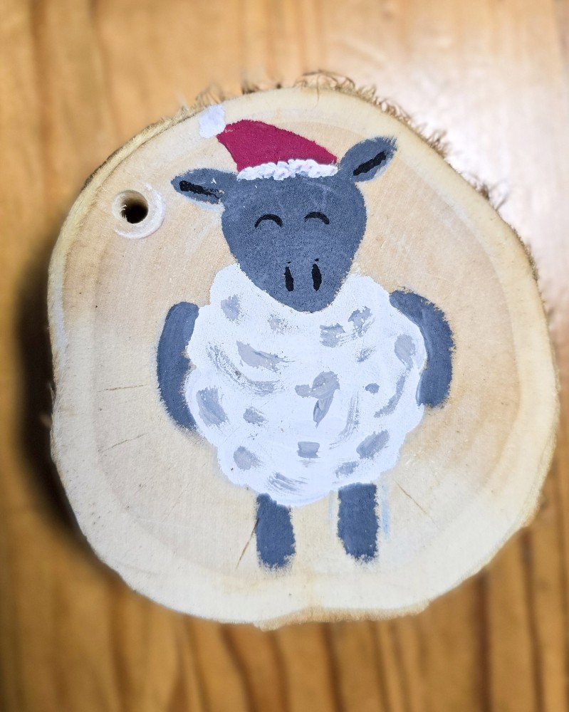Eine bemalte Deko-Holzscheibe mit einem Schaf mit Weihnachtsmütze